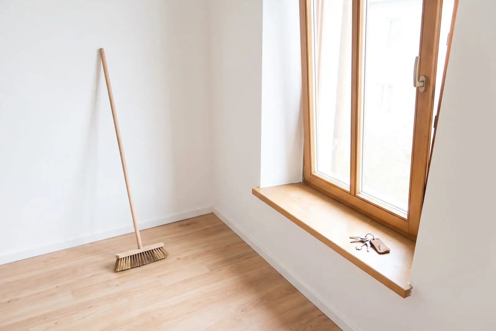 Leeres, frisch gefegtes Zimmer mit Besen in der Ecke und einem Schlüsselbund auf der Fensterbank