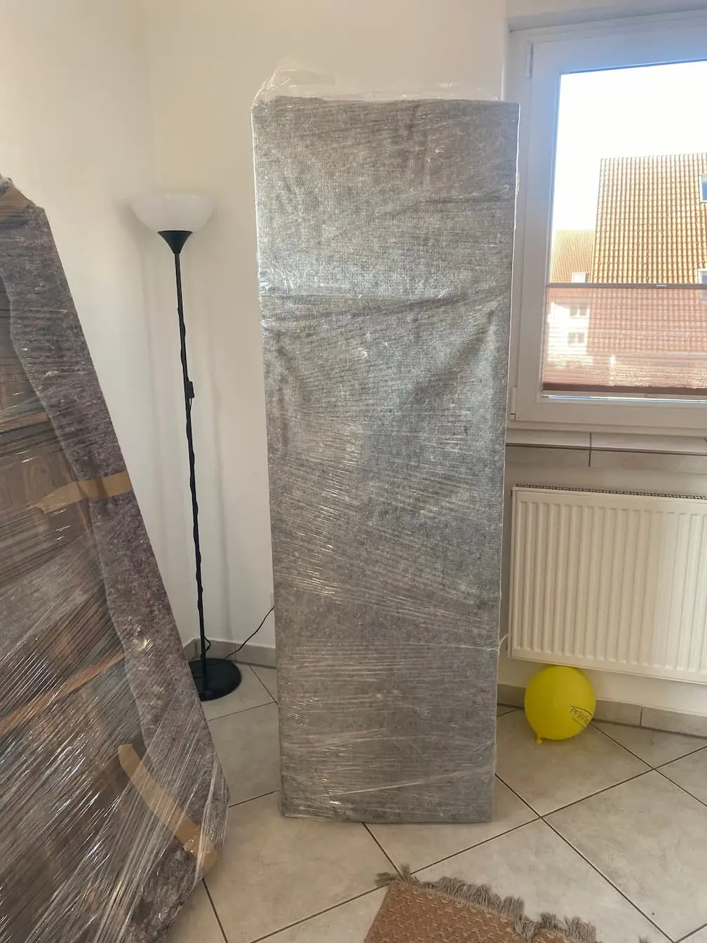 Ein hohes Schrankelement, in Decke und Folie gewickelt, steht aufrecht im Zimmer